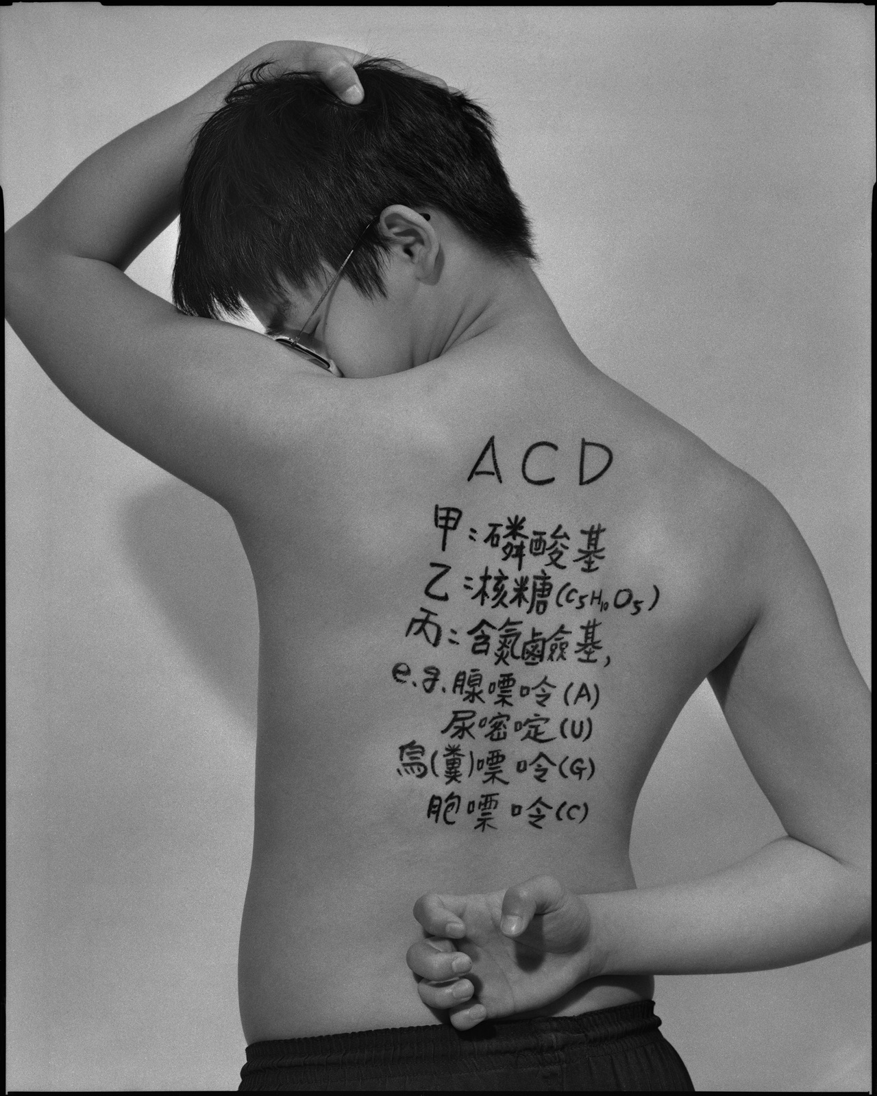 《答案》系列：黑白肖像，背面軀幹寫滿〈生物，2022〉考題手寫解答，雙手於頸後或背後交扣。