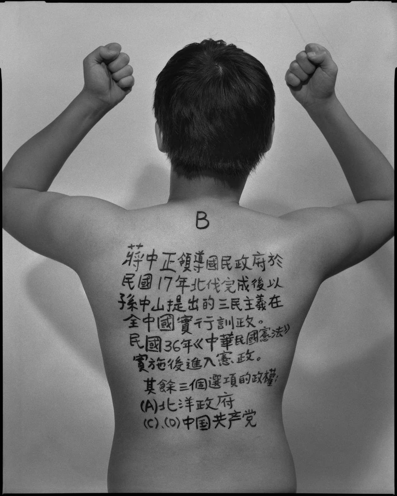 《答案》系列：黑白肖像，背面軀幹寫滿〈歷史，2024〉考題手寫解答，雙手於頸後或背後交扣。