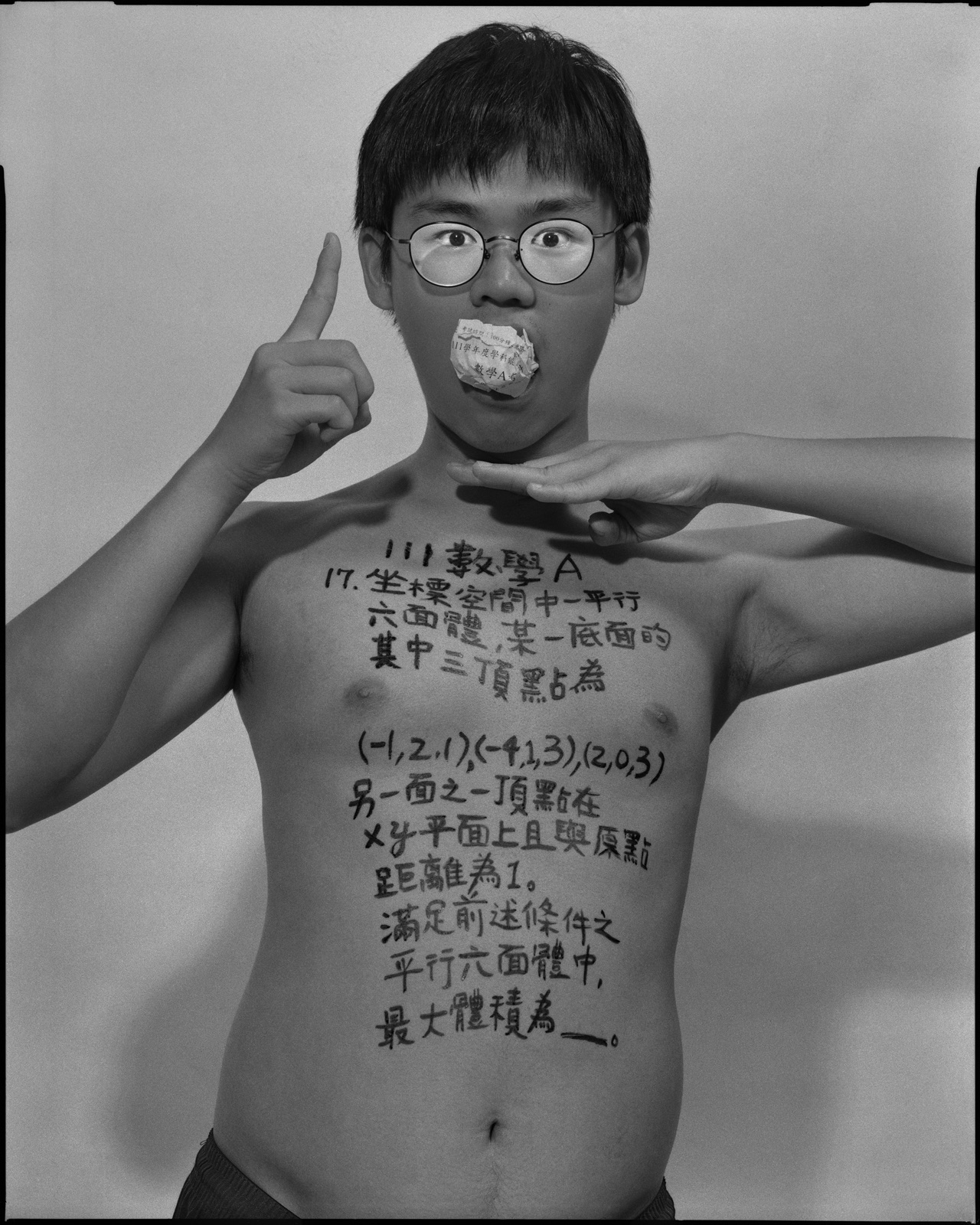 《答案》系列：黑白肖像，正面軀幹寫滿〈數學，2022〉考題手寫文字，口中塞著紙捲，雙手於臉部前交疊。
