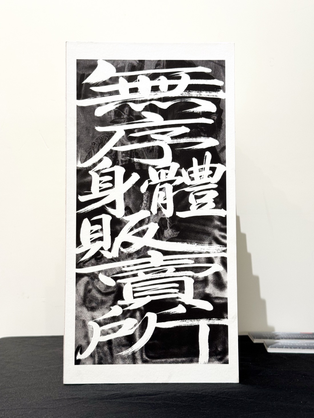 《無序身體販賣所》題名書法,白色筆觸書於深色底,立於展台。