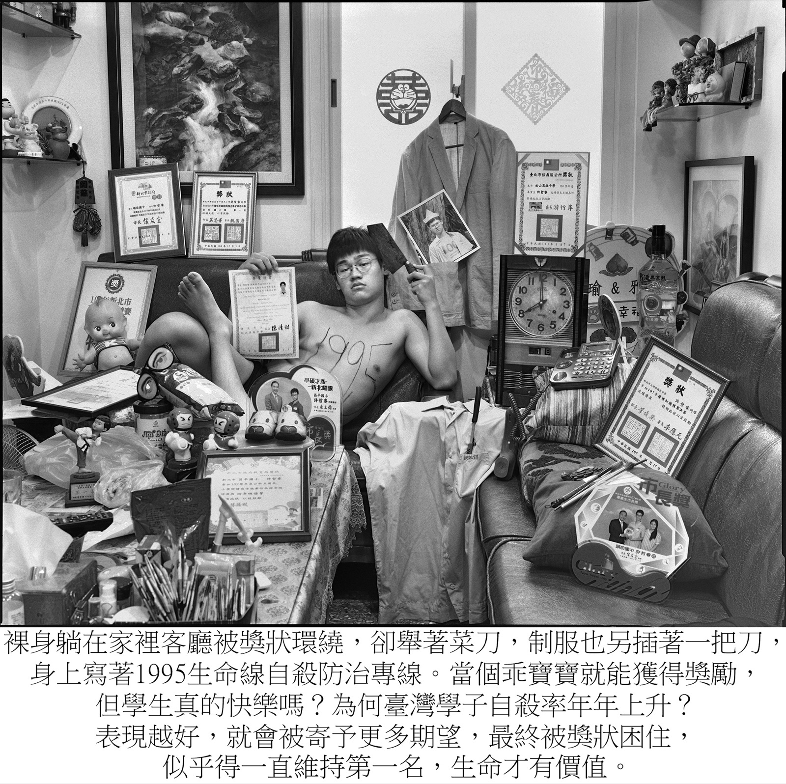 《乖寶寶 Good boy》裝置:藝術家裸身躺臥於堆滿獎狀獎盃的自宅客廳沙發,手持菜刀,身上書寫「1995」生命線字樣。
