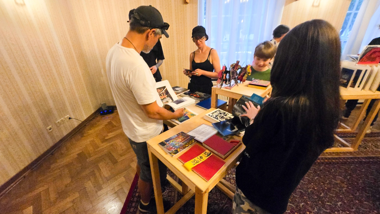 《複眼之島》羅茲展場：多位觀眾圍聚展桌翻閱藝術家手工書，含《無序身體販賣所》經摺裝。