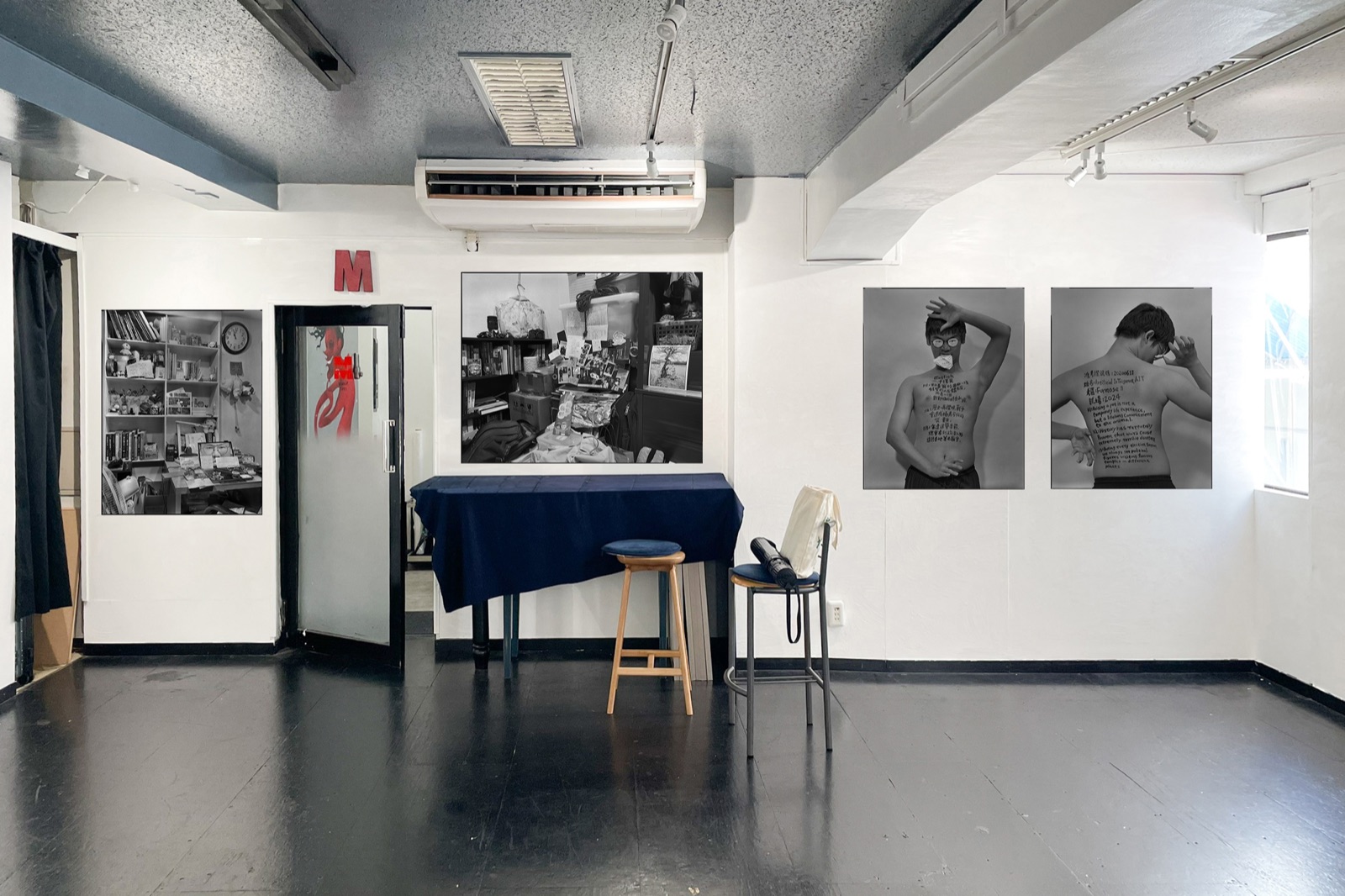 Place M 展場入口一景：牆上並列展出黑白肖像作品，中央擺設簽名桌與圓凳。